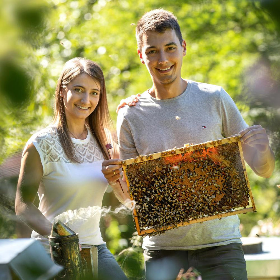 Stefanie und Simon Weber mit einer Bienenwabe an ihren Bienenstöcken